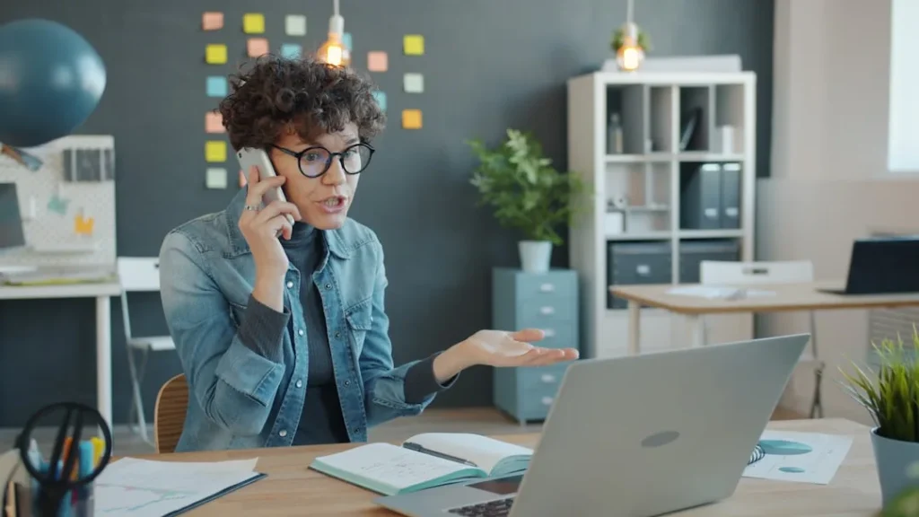Woman on phone frustrated by WooCommerce sales dropping on her laptop screen